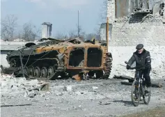  ?? (Alexander Ermochenko/Reuters) ?? A MAN RIDES a bicycle past a charred armored vehicle during Russia’s attack on the separatist-controlled town of Volnovakha in the Donetsk region of Ukraine in March.