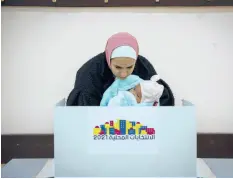  ?? MAJDI MOHAMMED/AP ?? A woman holds a baby as she votes during municipal elections Saturday in the West Bank.