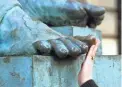  ?? MARTIN CLEAVER/AP ?? A woman touches the toe of the bronze statue of Scottish philosophe­r David Hume in Edinburgh. Passers-by rub the shiny big toe for luck.