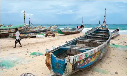  ?? Photograph: SEYLLOU/AFP/Getty Images ?? A man walks past pirogues in Fass Boye, the type of fishing boat which capsized off the coast of Cape Verde, killing scores of people.