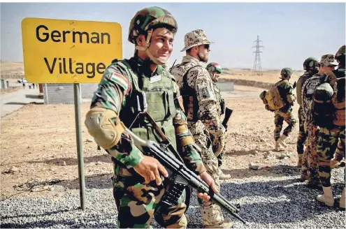  ?? FOTO: DPA ?? Angehörige der kurdischen Peschmerga und Soldaten der Bundeswehr in der Ausbildung­seinrichtu­ng Bnaslawa nahe Erbil im Nordirak vor dem Übungsdorf „German Village“, wo der Häuserkamp­f geübt wird. Neuerdings trainieren die Deutschen jedoch nur noch kurdische Ausbilder.