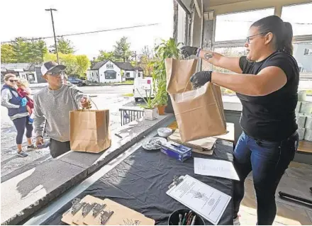  ?? KENNETH K. LAM/BALTIMORE SUN ?? Colleen Fox, right, a manager at Vida Taco Bar's Annapolis restaurant, hands bags of grocery items to customer Rick Sowell in Severna Park.