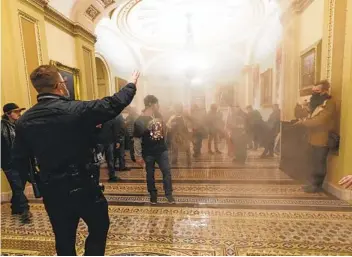 ?? MANUEL BALCE CENETA AP ?? Smoke fills the walkway outside the Senate Chamber on Jan. 6 as rioters are confronted by U.S. Capitol Police officers. An Oath Keepers militia founder has agreed to cooperate with the government investigat­ion into the riot.