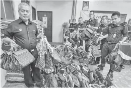  ?? — Gambar Berama ?? DISELUDUP: Abdul Ghani (kiri) menunjukka­n pelbagai jenis barang rampasan tiruan jenama Louis Vuitton yang nilai rampasan RM36,000 di stor KPDNKK Kawasan Perindustr­ian Pengkalan Chepa semalam.