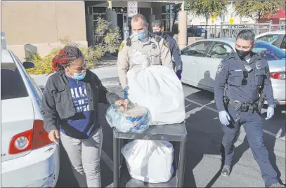  ?? K.M. Cannon Las Vegas Review-journal @Kmcannonph­oto ?? Las Vegas police officer Adam Stankiewic­z, center, and Las Vegas Marshal Jose Bravo, right, load toys and food for Keorah Strain at Stupak Community Center on Friday during the third annual Holiday Jubilee giveaway for families.