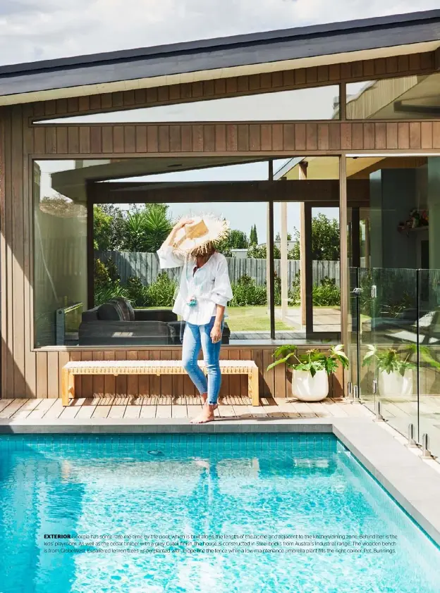  ??  ?? EXTERIOR Georgia has some rare me-time by the pool, which is built along the length of the home and adjacent to the kitchen/dining zone. Behind her is the kids’ playroom. As well as the cedar timber with a grey Cutek finish, the house is constructe­d in Steel bricks from Austral’s Industrial range. The wooden bench is from GlobeWest. Espaliered lemon trees underplant­ed with liriope line the fence while a low-maintenanc­e umbrella plant fills the right corner. Pot, Bunnings.