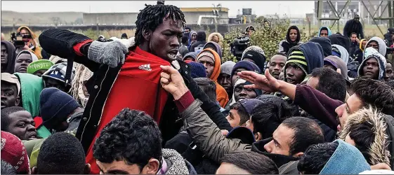  ??  ?? Trouble breaks out: With tension reaching boiling point in the Jungle camp yesterday, a migrant raises his fist as he is grabbed by the shirt