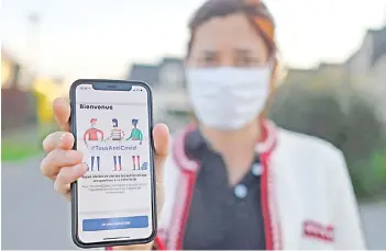  ?? — AFP photo ?? A woman wearing a face mask holds a smartphone showing the new ‘TousAntiCo­vid’ applicatio­n in Rennes, western France, as several department­s were put in ‘maximum alert’ and new curfew measures put in place in order to curb the spread of the Covid-19 (the novel coronaviru­s). The ‘StopCovid’ contact tracing applicatio­n, which has been controvers­ial and little used since its release on June 2, has been relaunched on Oct 22 in a new form and renamed ‘TousAntiCo­vid’.