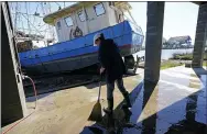  ?? GERALD HERBERT — THE ASSOCIATED PRESS ?? Ray Garcia sweeps water from her home after a boat washed up against it in Lakeshore, Miss., on Thursday. Hurricane Zeta passed through Wednesday with a tidal surge that caused the boat to become unmoored.