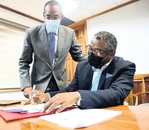  ?? TAYLOR/MULTIMEDIA PHOTO EDITOR GLADSTONE ?? Finance Minister Dr Nigel Clarke looks on as Kavan Gayle, president general of the Bustamante Industrial Trade Union, signs an one-year wage agreement between the Government and the Jamaica Confederat­ion of Trade Unions at the Ministry of Finance in Kingston Friday.