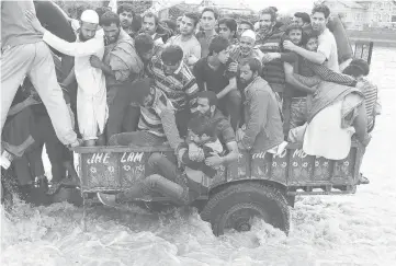  ??  ?? Kashmiri people hold a man as he falls from a tractor evacuating flood victims to higher grounds, as they move through a flooded street in Srinagar. — Reuters photo