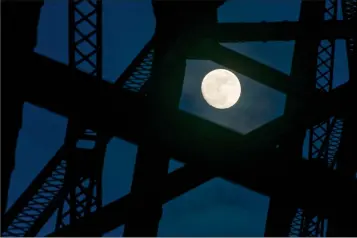  ?? Herald photo by Ian Martens ?? The nearly full moon peeks from between the metal girders of the High Level Bridge Monday evening in the river bottom. Early Wednesday morning will see a rare convergenc­e of three lunar phenomena being called a Super Blue Blood Moon. @IMartensHe­rald