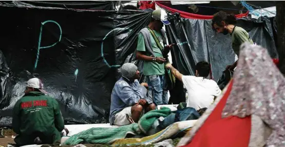  ??  ?? Usuários de drogas se concentram em frente a barracas com a sigla da facção criminosa PCC, na praça Princesa Isabel, no centro de São Paulo