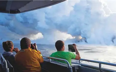  ?? AP ?? People take pictures as lava enters the ocean near Pahoa, Hawaii, on Sunday. Laze — a term combining the words ‘lava’ and ‘haze’ — is created when erupting lava, which can reach 2,000 degrees Fahrenheit, reacts with seawater.