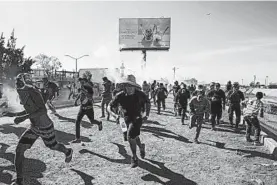  ?? GUILLERMO ARIAS/GETTY-AFP ?? Migrants fled Sunday after Border Patrol fired tear gas at them along the Tijuana River.