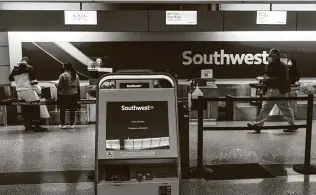  ?? David Paul Morris / Bloomberg ?? Travelers wearing protective masks speak with an attendant at the Southwest Airlines check-in area at Oakland Internatio­nal Airport in California last month.