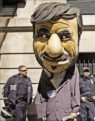  ??  ?? NYPD officers look on as man dressed in an oversized mask of Mahmoud Ahmadineja­d protests the Iranian strongman outside the Warwick Hotel.