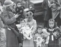  ??  ?? In this March 30, 1942, file photo, Cpl. George Bushy (left), a member of the military guard which supervised the departure of 237 Japanese people for California, holds the youngest child of Shigeho Kitamoto (center) as she and her children are...