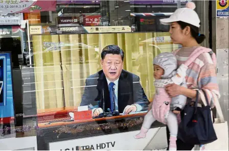  ??  ?? On the air: A woman carrying her baby past a television in New Taipei City showing Xi’s speech. — AFP