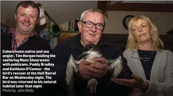  ?? Photo by John Reidy ?? Cahercivee­n native and sea angler, Tim Horgan holding the seafaring Manx Shearwater with publicans, Paddy Bradley and Kathleen O’Connor - the bird’s rescuer at the Half Barrel Bar on Wednesday night. The bird was returned to his natural habitat later...