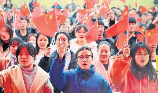  ?? AFP/GETTY IMAGES ?? Students wave flags as they watch live coverage of a speech in Beijing by China's President Xi Jinping in December.