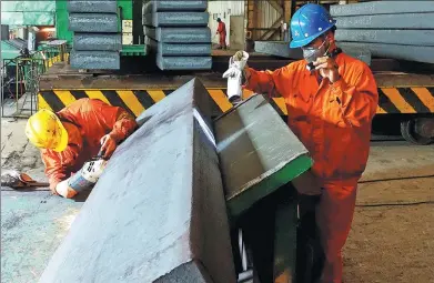  ?? LIU DEBIN / FOR CHINA DAILY ?? Workers at Dalian Special Steel Products Co Ltd, part of Dongbei Special Steel Group, check the surface of a flat stab grinding mold.