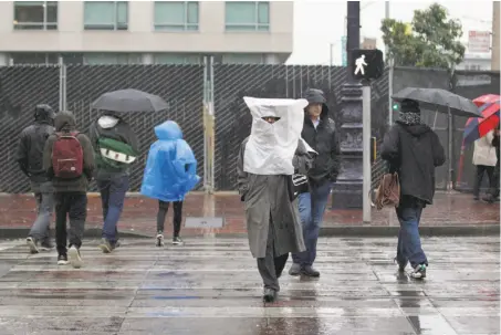  ?? Lea Suzuki / The Chronicle ?? Richard Toyama crosses Market Street on his way to the library wearing a rain hat made of a paper bag and a plastic bag.