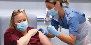  ??  ?? Health service: Vivien McKay, Clinical Nurse Manager at the Western General Hospital in Edinburgh, rolls up her sleeve to be given her jab from a colleague