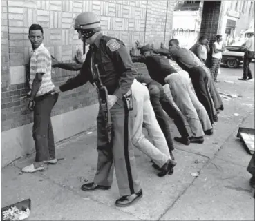  ?? FILE — THE ASSOCIATED PRESS ?? In this 1967 photo, a Michigan State police officer searches a youth on Detroit’s 12th Street where looting was still in progress after the previous day’s rioting. The last surviving member of the Kerner Commission says he remains haunted that the...