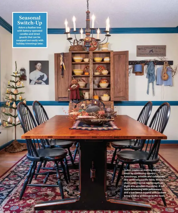  ??  ?? JoAnn creates an inviting dining room by combining country furnishing­s, artwork and collectibl­es. She centered a trestle table, Windsor chairs and Oriental rug beneath an eight-arm wooden chandelier. A tall hutch brimming with yellowware and a low bench topped with baskets bring a folksy ambience to the room.