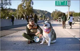  ?? PHOTO BY ANDY HOLZMAN ?? Frank Coronado sits along the 110Freeway along with his husky-type dog, Sequoia, on Sunday during the ArroyoFest open-streets event between Los Angeles and Pasadena.