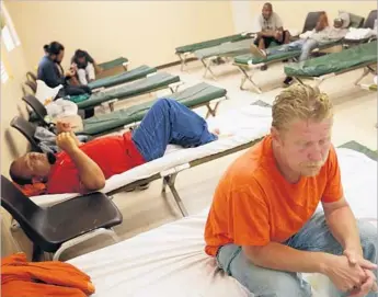  ?? Photograph­s by Genaro Molina Los Angeles Times ?? MIKE BASS, 51, right, and other homeless men wait to bed down Wednesday at the Lancaster Community Shelter. After years of deficit spending, the nonprofit behind the Antelope Valley facility will shut its doors.