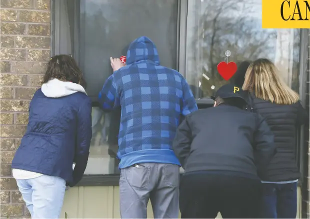  ?? VERONICA HENRI / POSTMEDIA NEWS ?? Family members look through a window as they visit a resident at Orchard Villa long-term care home in Pickering, Ont., earlier this month.