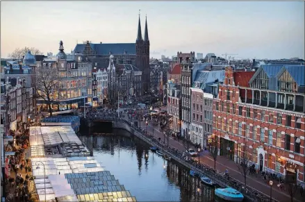  ?? JASPER JUINEN/BLOOMBERG ?? Flower stalls (left) float illuminate­d on a canal at the Bloemenmar­kt as the Kalverton retail mall sits on the opposite bank in Amsterdam in 2013.