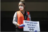  ??  ?? Cindy Mamenta, a licensed vocational nurse, holds a sign she shows to patients in their cars at the entrance to the outdoor clinic at the Sutter Health Palo Alto Medical Foundation in San Carlos.