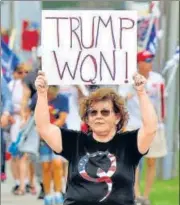  ?? REUTERS ?? Donald Trump speaks with reporters at the North Carolina convention dinner in Greenville; a supporter (right) in a QAnon shirt displays a banner.