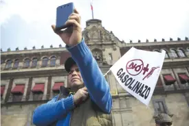  ??  ?? MEXICO CITY: A man holding a flag that reads “No more gasoline price hikes” films other protestors in as they chant anti-government slogans in front of the National Palace. — AP