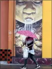  ?? JANE TYSKA — STAFF PHOTOGRAPH­ER ?? A pedestrian tries to stay dry as she walks past a mural during a rainfall along Fruitvale Avenue in Oakland on Tuesday.