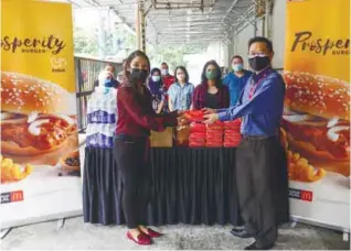  ?? ASYRAF RASID/THESUN ?? Aini (left) handing over the first chicken Prosperity Burger to Ong during McDonald’s Malaysia’s visit to theSun’s office. –