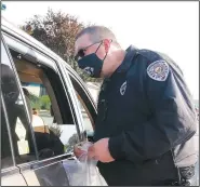  ?? (NWA Democrat-Gazette/Lynn Kutter) ?? Jimmy Brotherton, Farmington school resource officer, hands out police water bottles, bracelets, stickers, a coloring book and books to children during the fire safety event.