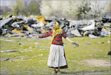 ?? Vadim Ghirda Associated Press ?? IN SINTESTI village, a woman waits as Romania’s National Environmen­tal Guard carries out a raid. The illegal burning of toxic materials to sell the metal seems like the only means of survival for some in the slums.