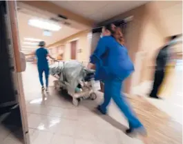  ?? GERALD HERBERT/AP ?? Staffers transfer a dead COVID-19 patient to a loading dock to hand off to a funeral home in Shreveport, La. A federal program reimburses families for funeral costs.