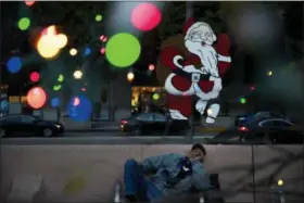  ?? JAE C. HONG — THE ASSOCIATED PRESS ?? Homeless man Alonzo Harrison, 47, takes a nap on a bench at Pershing Square decorated with Christmas lights in the background in Los Angeles.