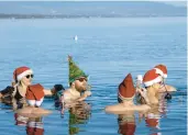  ?? MARTIAL TREZZINI/KEYSTONE ?? People drink as they swim with Santa hats in the frigid water Sunday, Christmas Eve, in Lake Leman at Bains des Paquis in Geneva, Switzerlan­d.