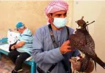  ??  ?? A mask-clad falconer holds a falcon near tourists at the historic Al-Fahidi neighborho­od of Dubai.