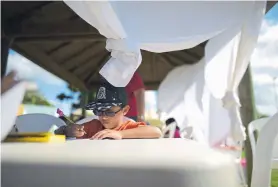  ??  ?? Andres Vazquez, a 6-year-old kindergart­en student, works at a plastic table set up under a gazebo, where his teacher from the Martin G. Brumbaugh School is conducting class at a municipal athletic park in Santa Isabel, Puerto Rico.