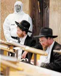  ?? ARIEL SCHALIT THE ASSOCIATED PRESS ?? An Israeli police officer wearing protective gear waits to detain ultra-Orthodox men as they pray in a synagogue in defiance of the government’s COVID-19 guidelines in Bnei Brak on Thursday.