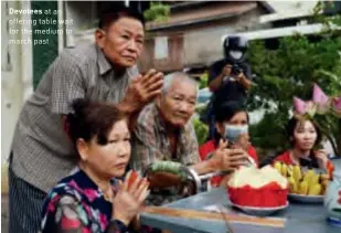  ??  ?? Devotees at an offering table wait for the medium to march past