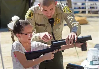  ?? Dan Watson/The Signal ?? Emmy Tohill, 8, gets instructio­ns from Deputy Rafael Velez as she prepares to fire a rubber projectile from a launcher during the Fun in the Sun Chili Cook-off held in Castaic on Saturday.