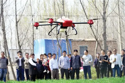  ??  ?? Villagers look on as an agricultur­al drone is used to spray pesticide on crops in a village in east China’s Shandong province. (AFP)